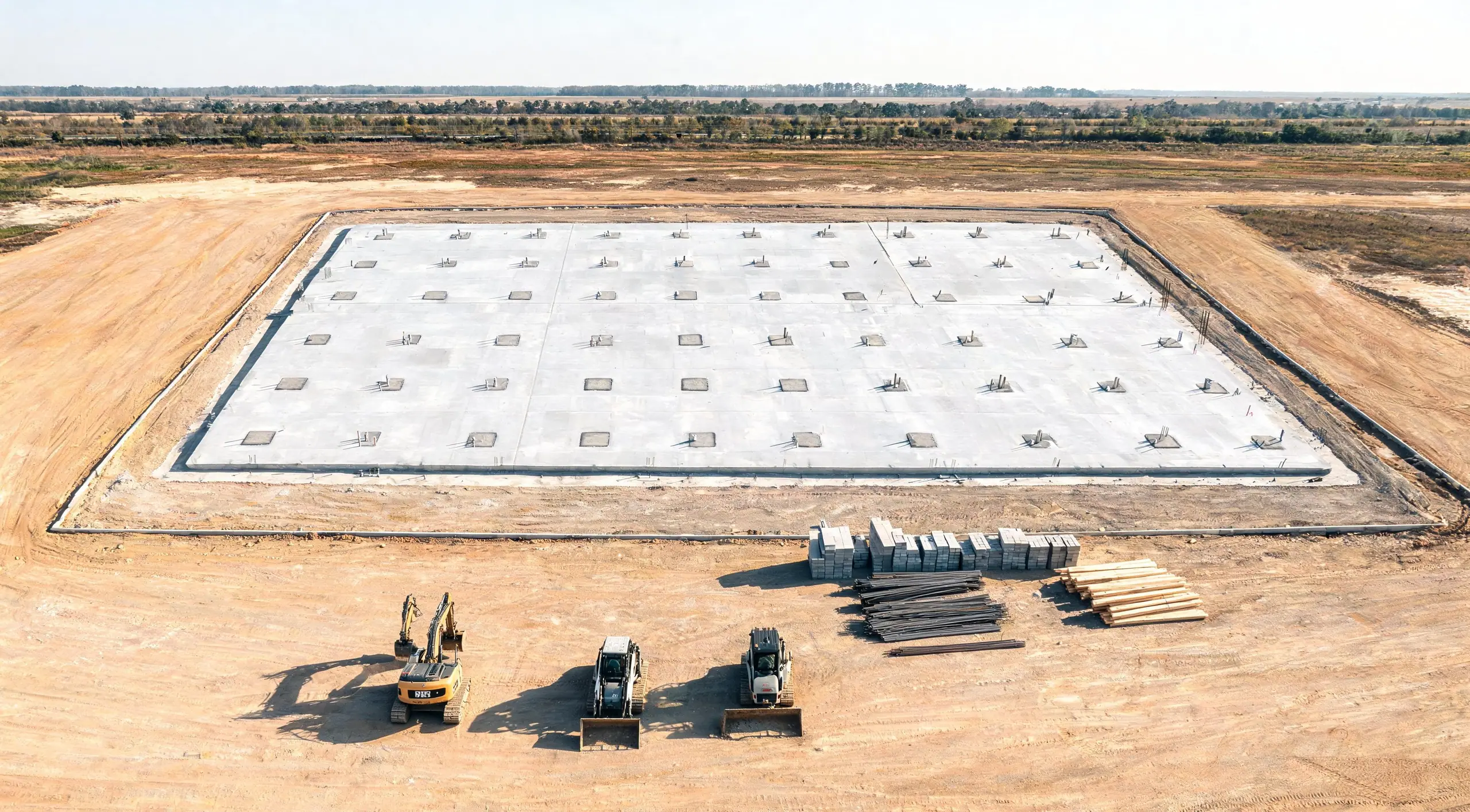 Aerial view of a new concrete foundation slab with column pads on a graded site