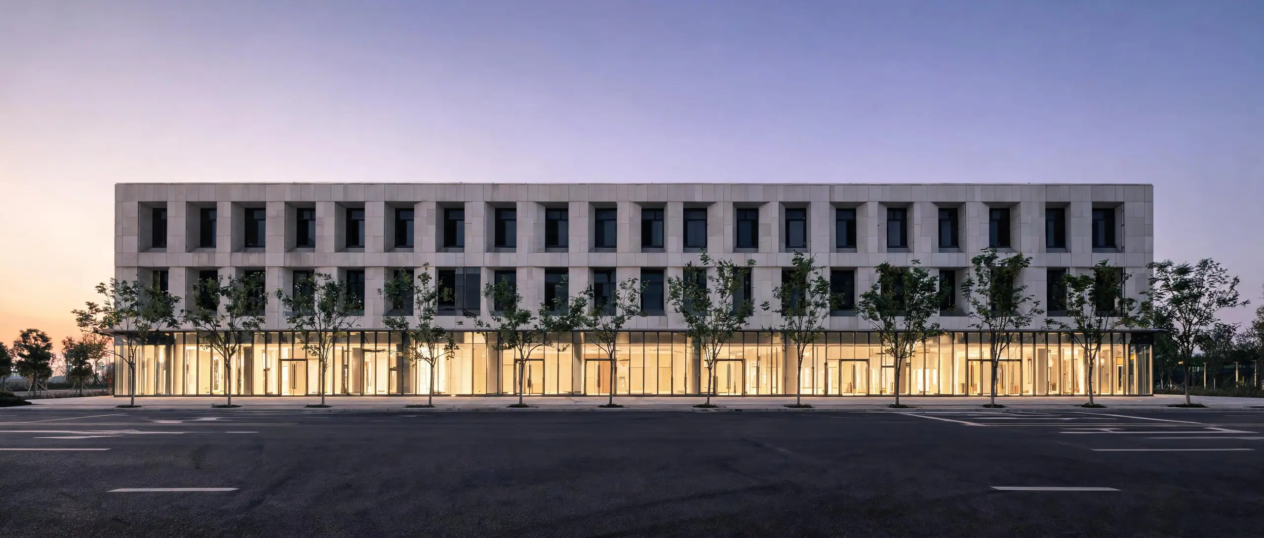 A three-story mixed-use building at dusk with lit ground-floor glass