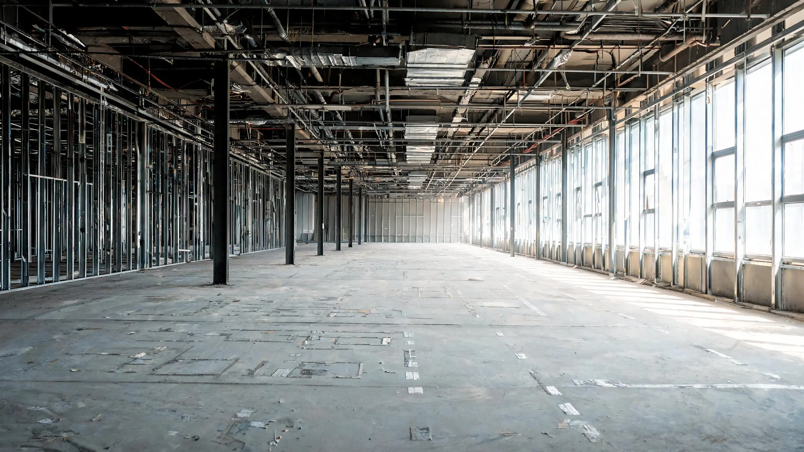 An office floor after interior demolition, bare concrete, exposed ceiling and stripped stud walls