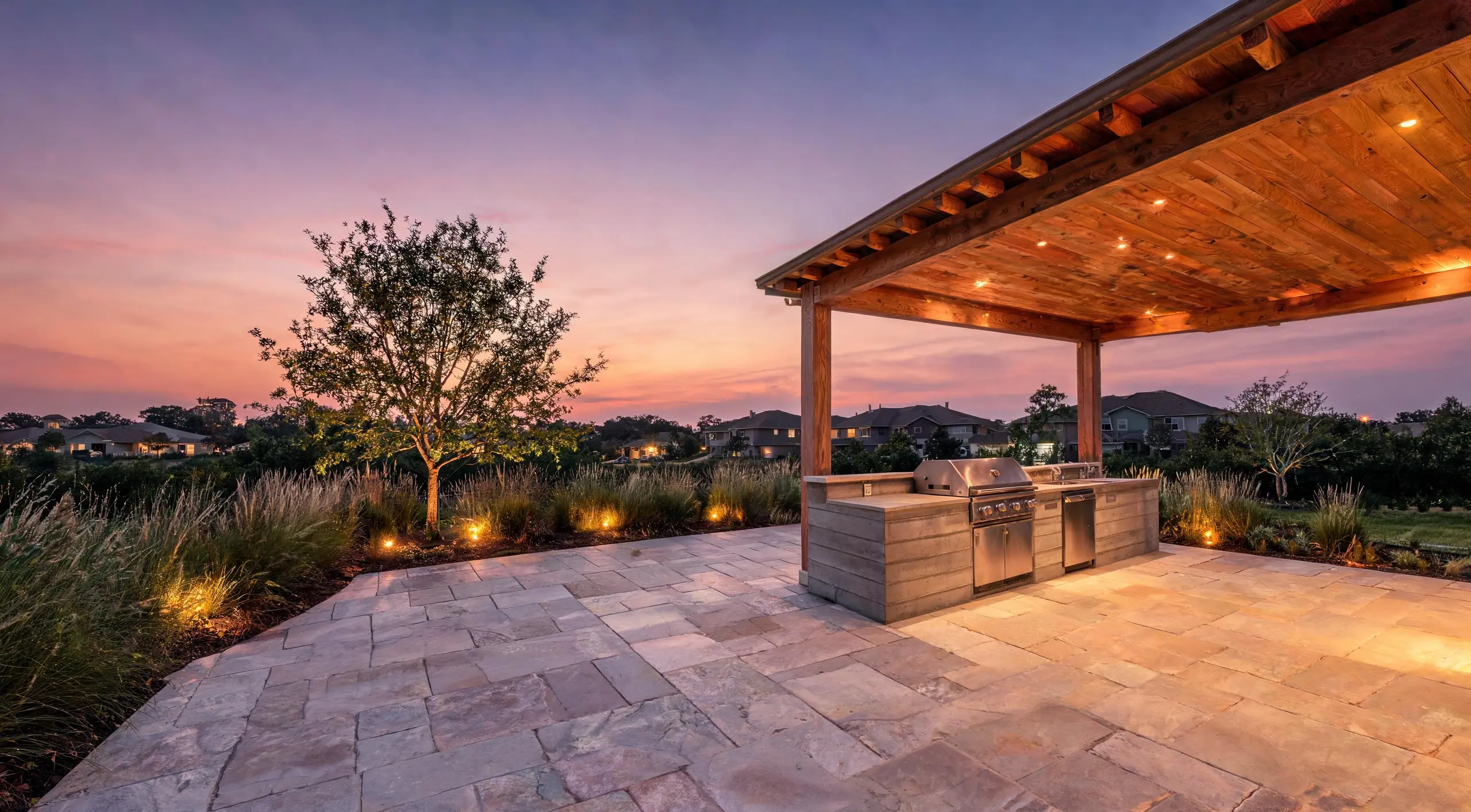A covered patio with an outdoor kitchen and limestone terrace at dusk