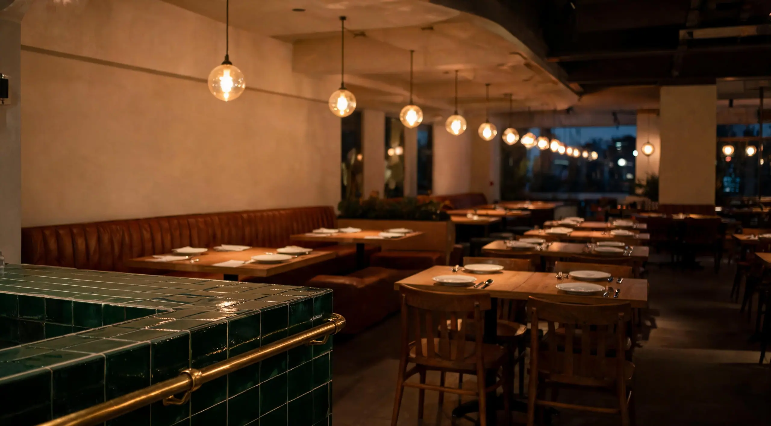 An empty finished restaurant with a green tile bar, brass rail, oak tables and leather banquettes