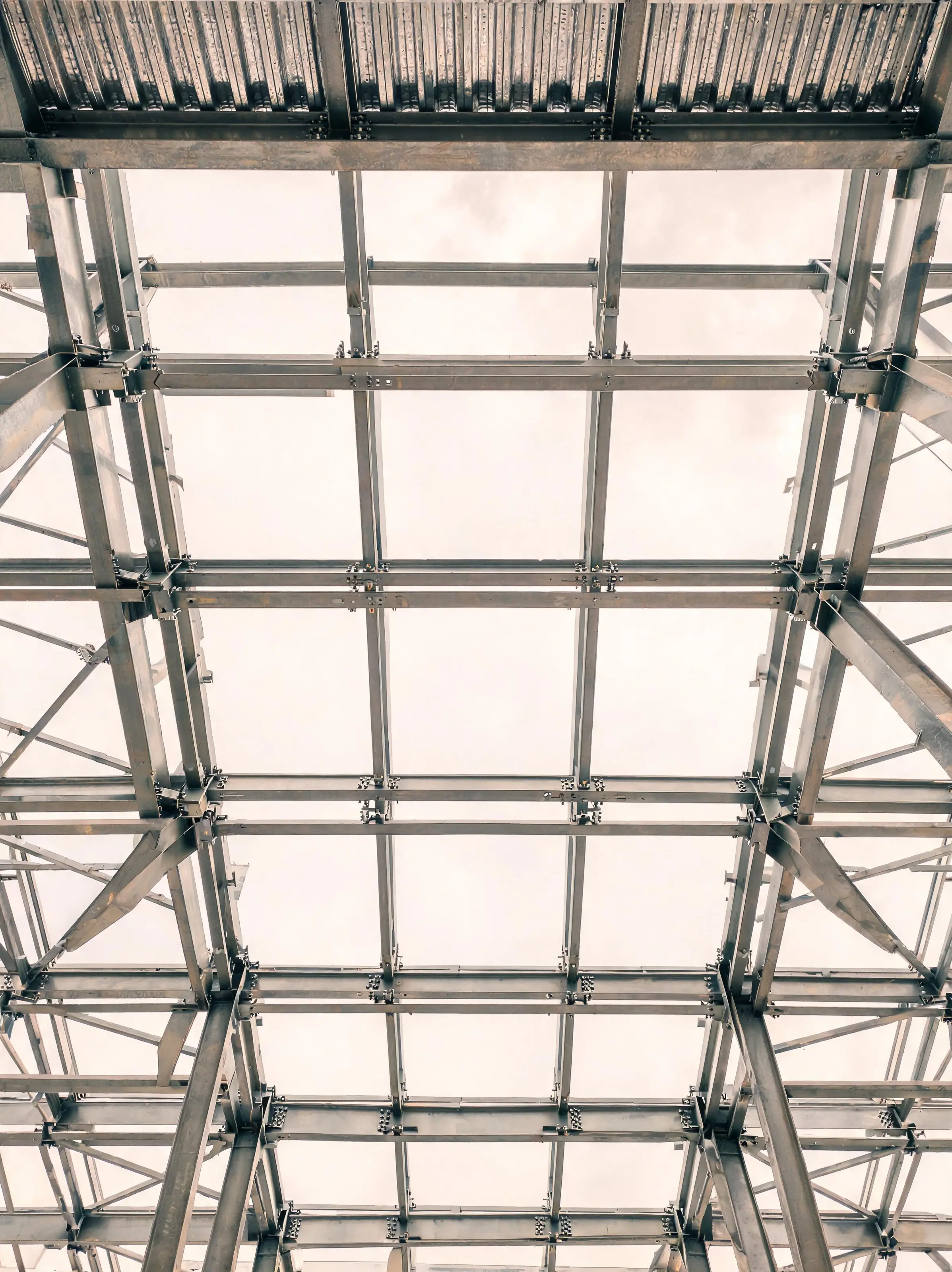 Looking up through a structural steel frame against a pale sky